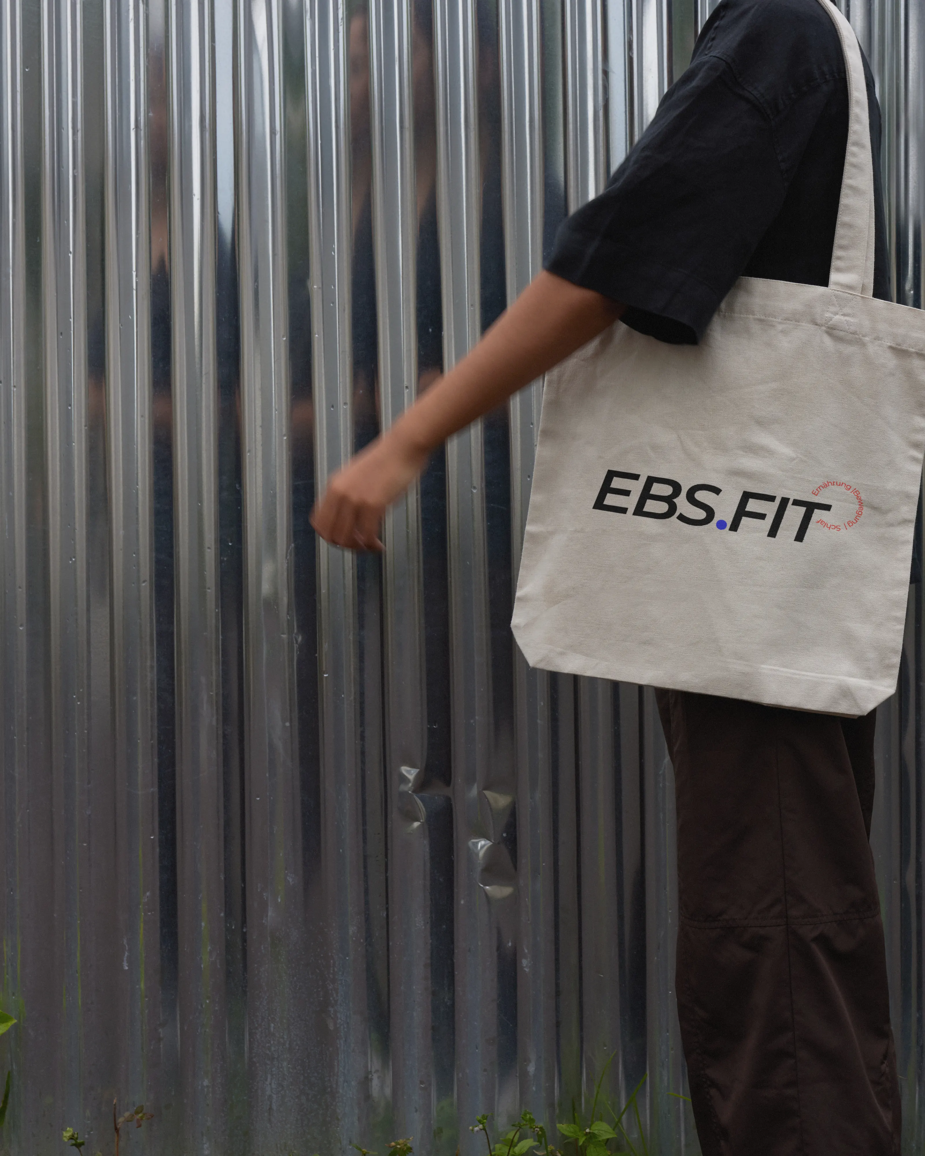 Stofftasche mit dem Logo EBS.FIT vor einer Wellblechwand, madea