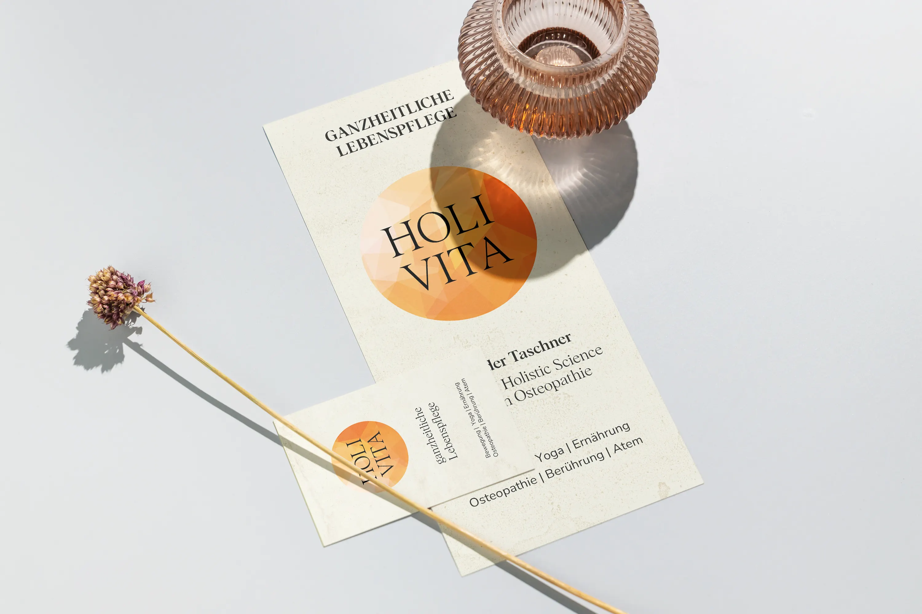 Folder und Visitenkarte Holivita neben einer Vase mit Trockenblume, madea