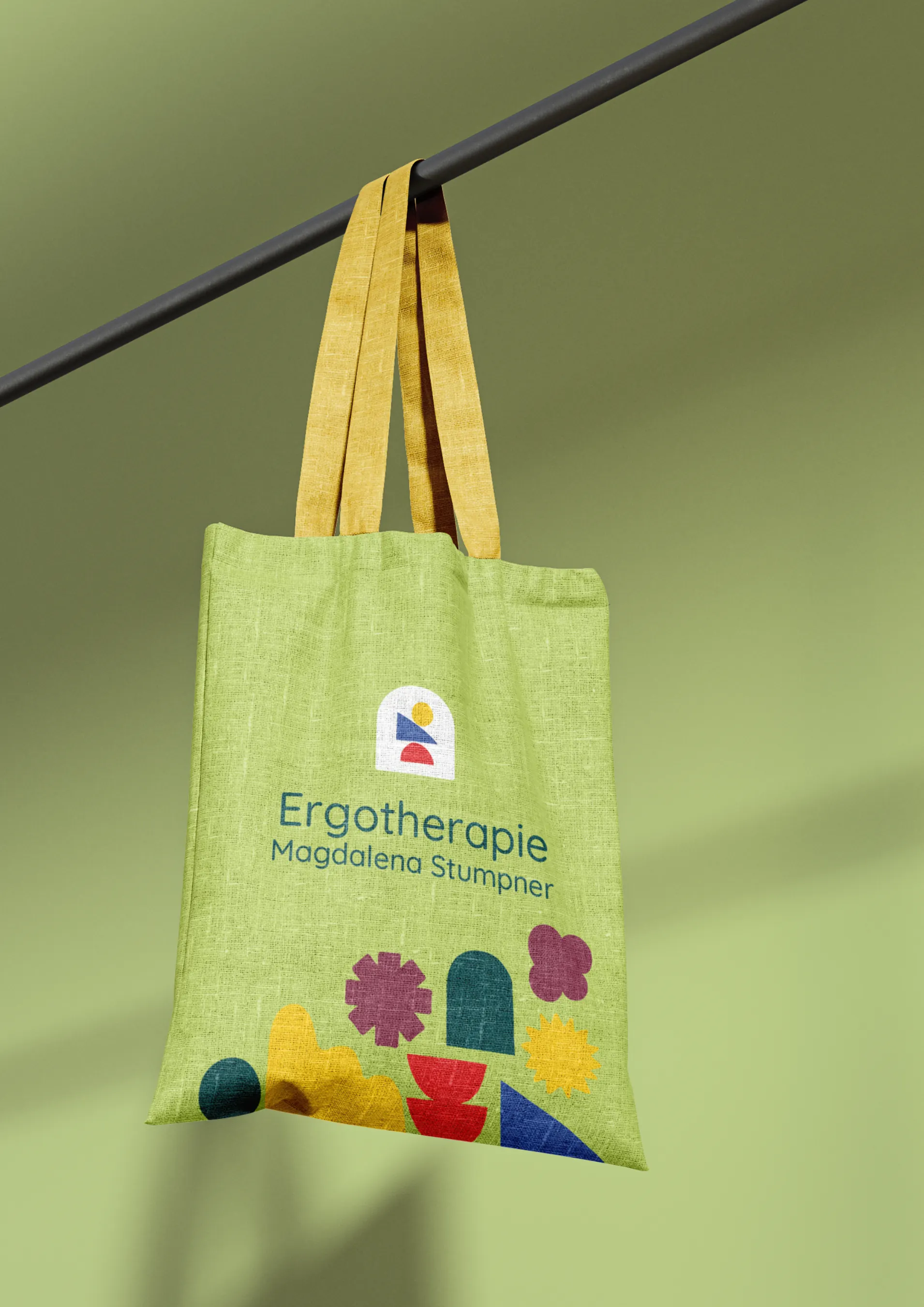Grüne Stofftasche mit Logo und bunten Formen an einer Stange, madea
